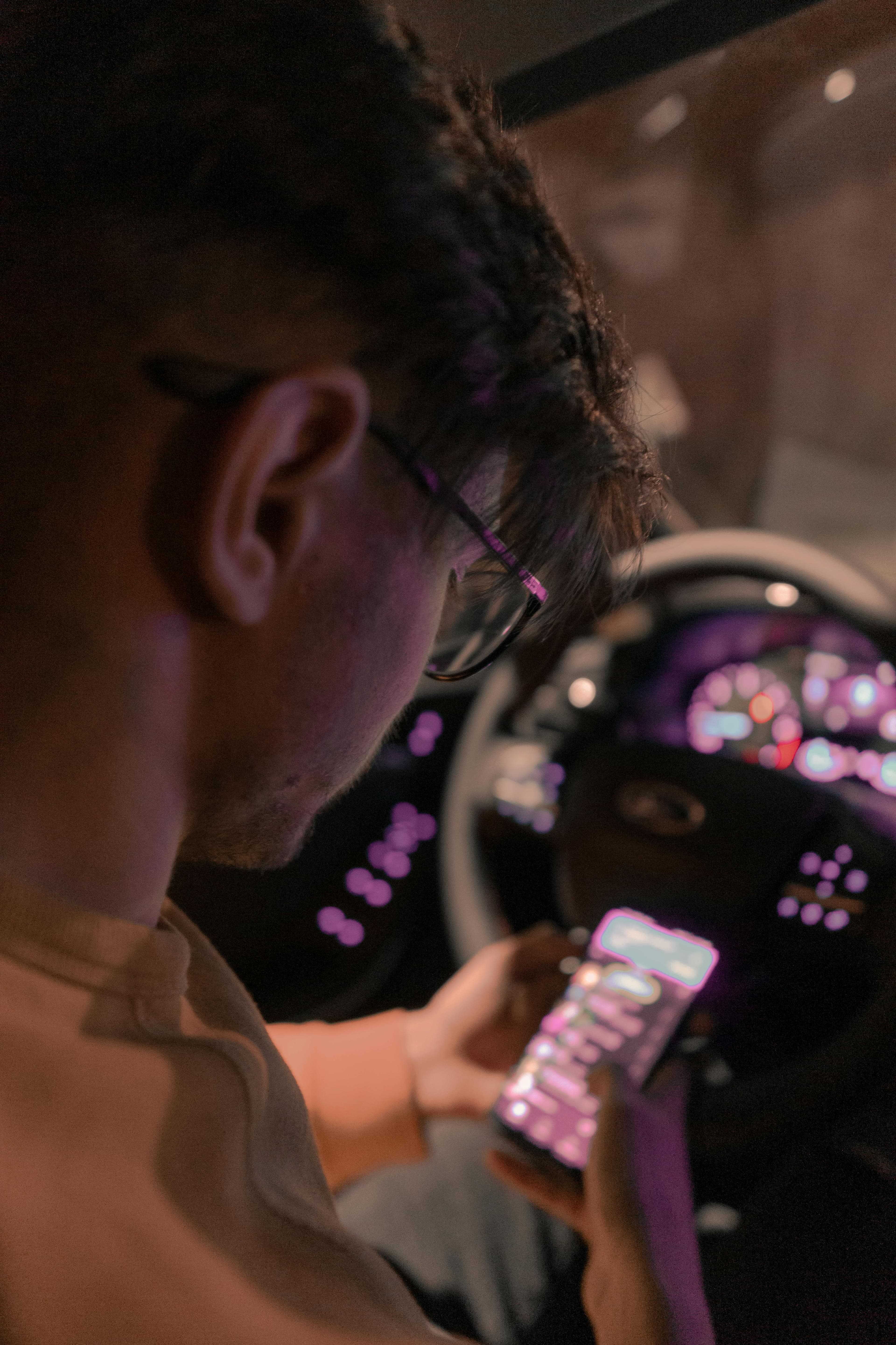 Persona usando su celular dentro de su auto mientras revisa información digital en la pantalla. Interior del vehículo con luces encendidas